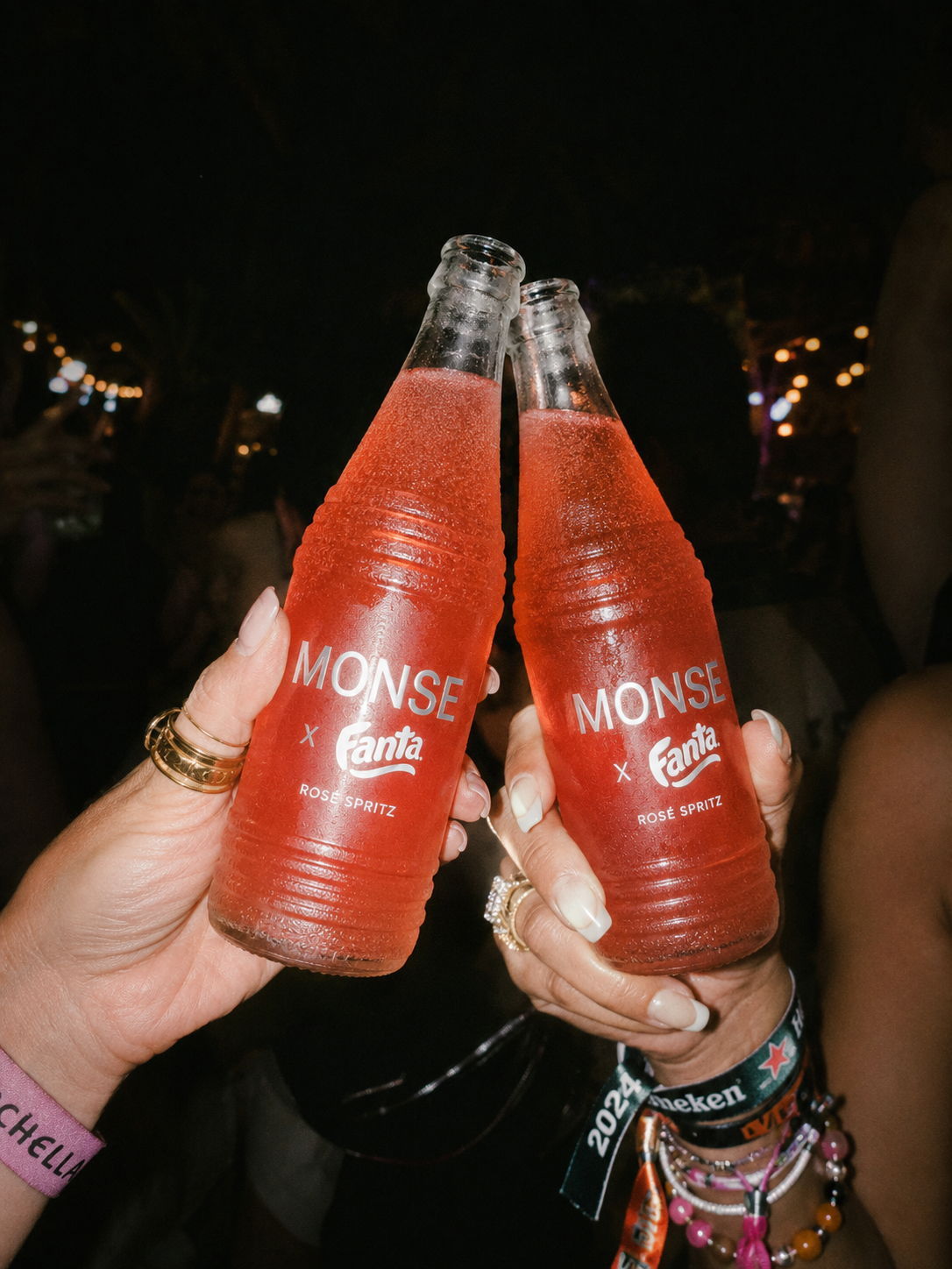 Two friends clinking MONSE x Fanta Rosé Spritz bottles at a festival at night